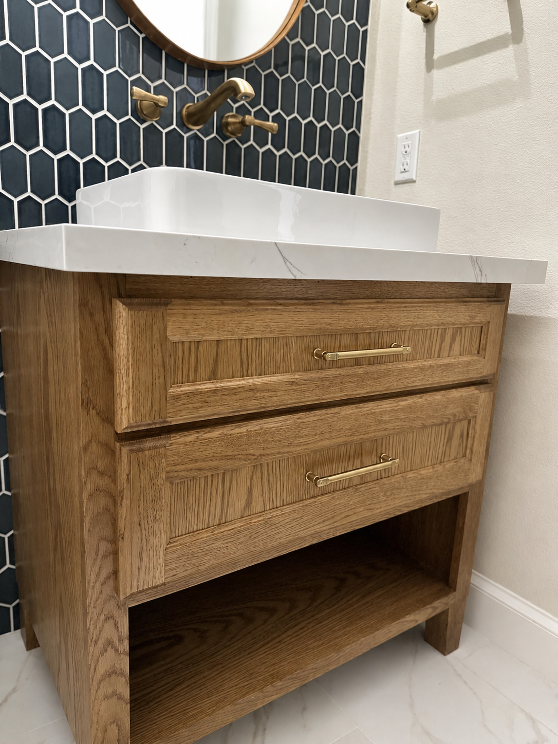 Custom oak vanity with marble countertop, vessel sink and brass hardware against a navy hex-tile wall.