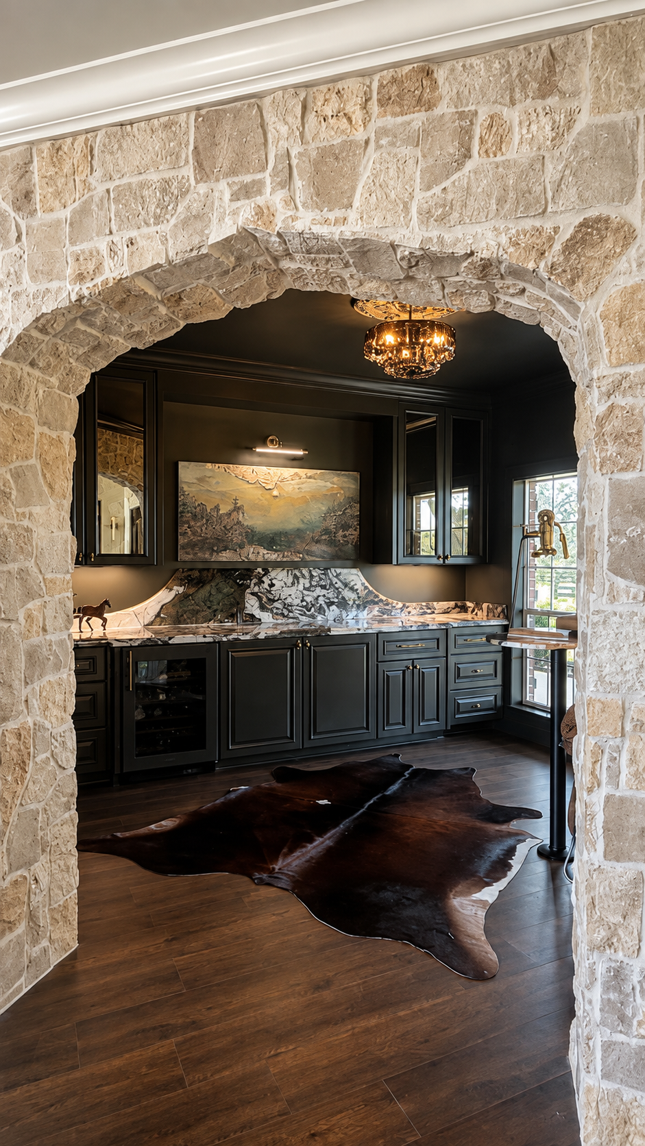 Wet bar seen through a rough limestone arch, with black cabinetry, dramatic stone counters and a hide rug on dark oak floors.