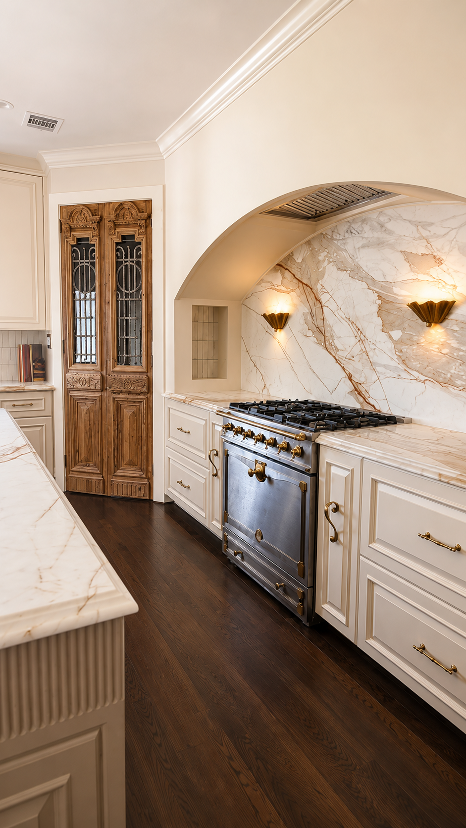 Traditional kitchen with cream cabinetry, an arched marble range alcove, antique carved pantry doors and dark oak floors.