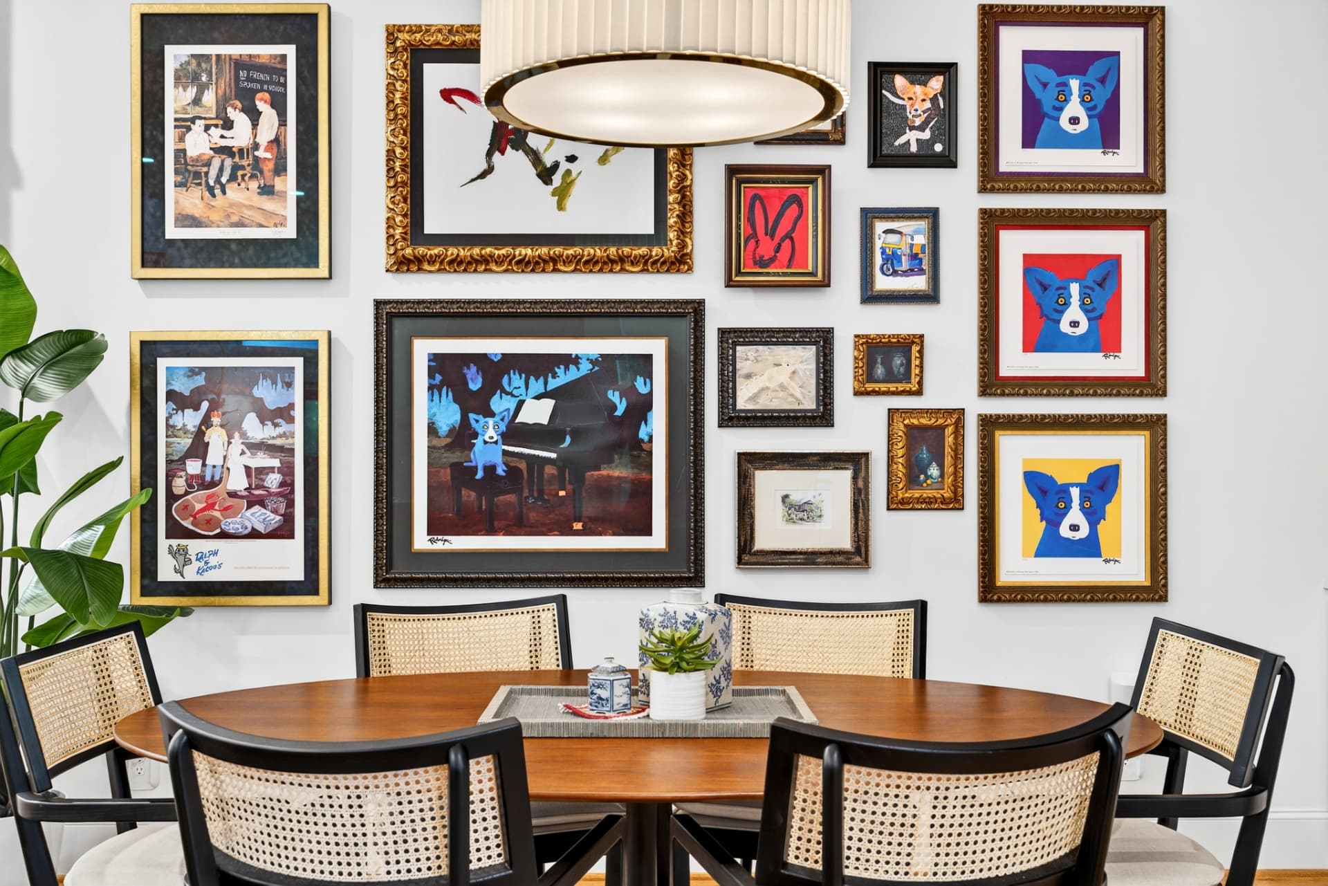 Breakfast area with a floor-to-ceiling gallery wall of framed art above a round walnut table with cane chairs.