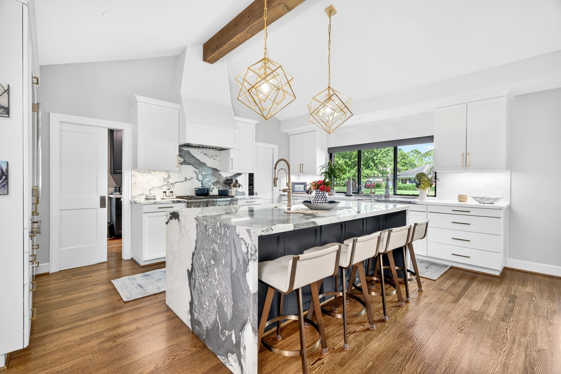 Renovated kitchen with a veined marble waterfall island, navy cabinetry and brass cube pendants.
