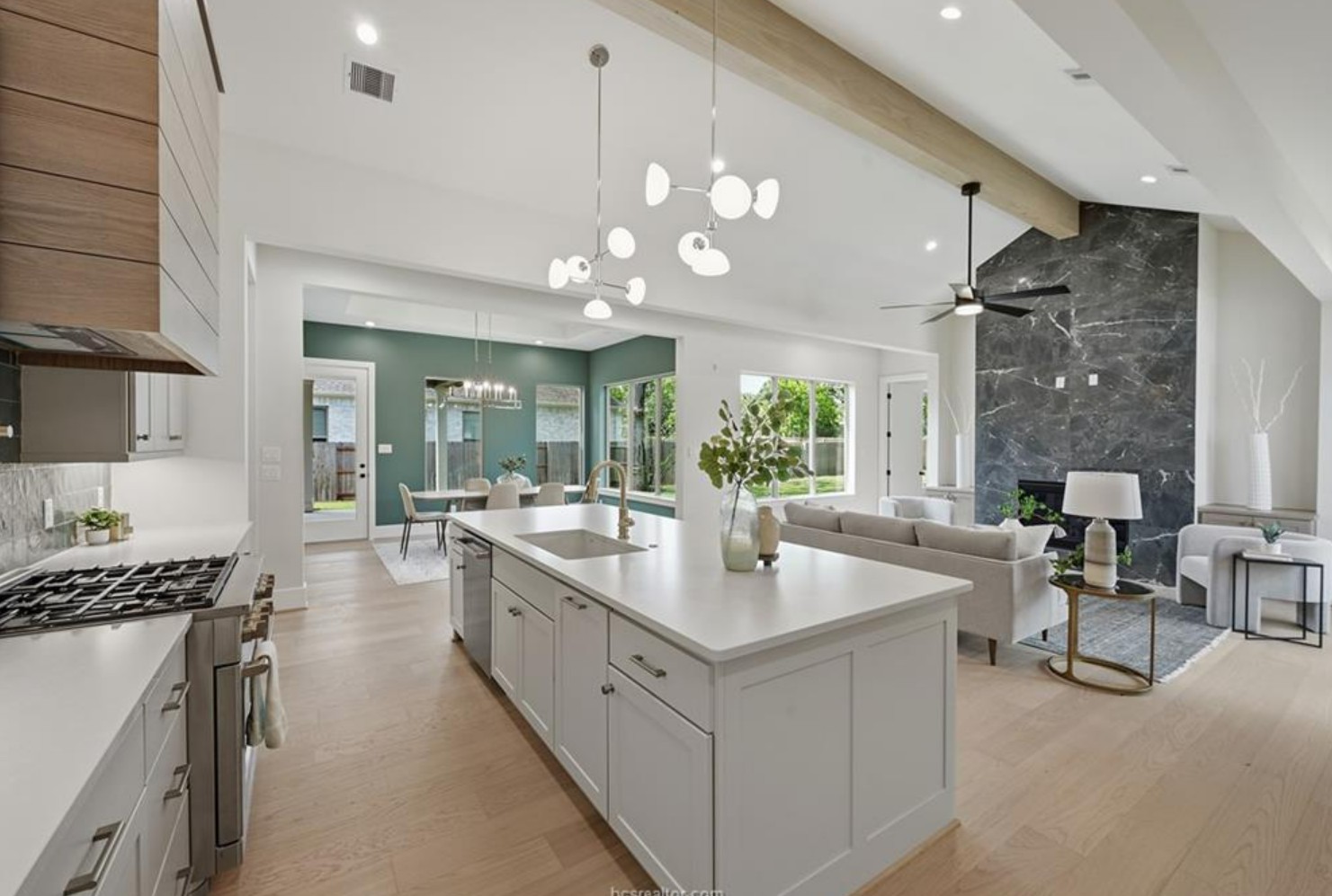 Open kitchen and living space with vaulted ceilings, wood beams and a dark marble fireplace surround.