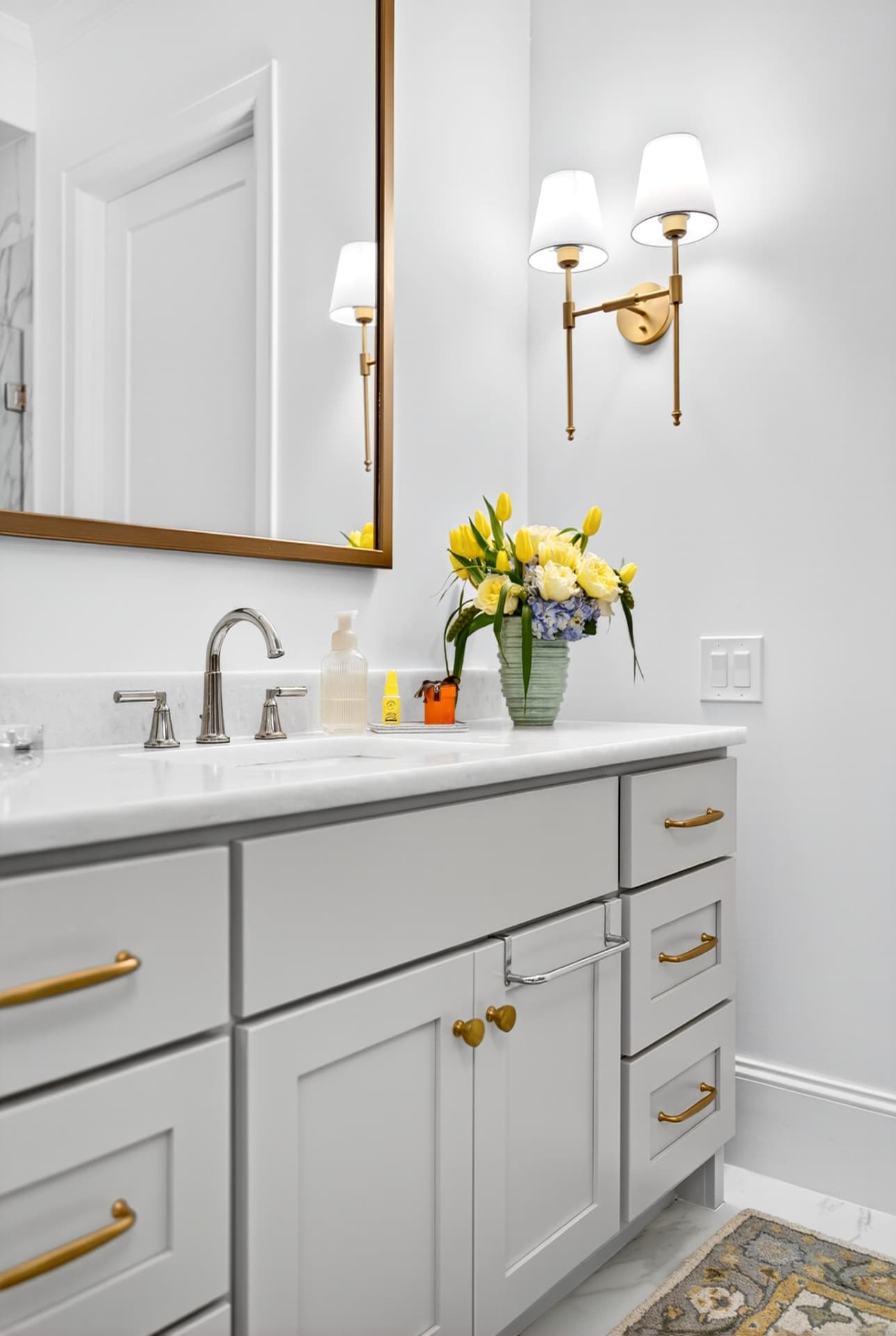 Guest bath vanity with grey cabinetry, brass pulls, marble counter and paired brass sconces.