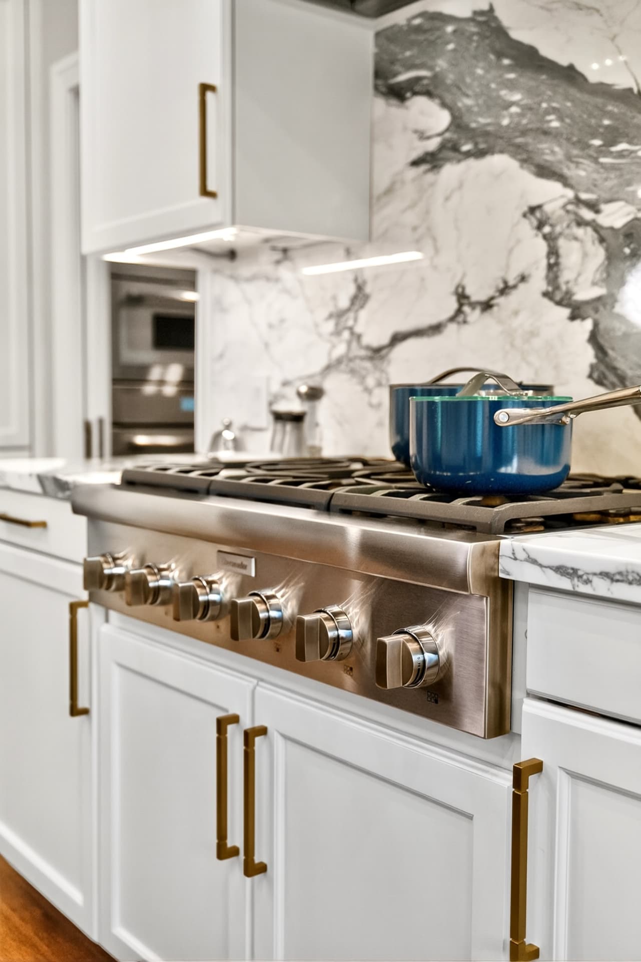 Detail of a professional range set against a dramatic veined marble slab backsplash with brass pulls.