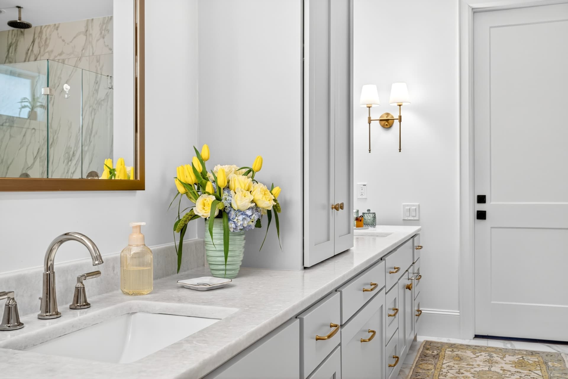 Primary bath vanity in soft grey with marble counters, brass hardware and a gold-framed mirror.