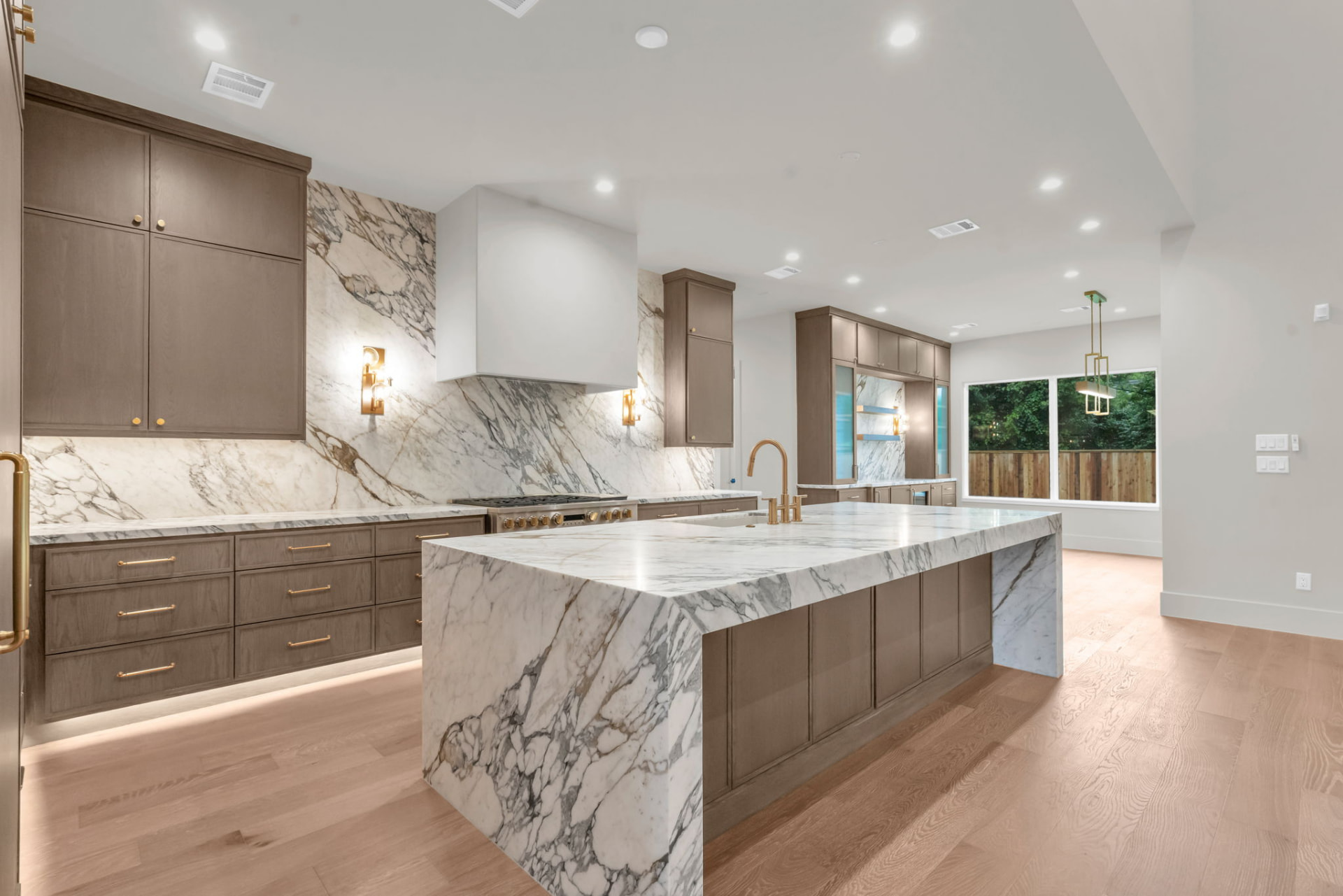 Open kitchen with quartersawn oak cabinetry, a full-height veined marble backsplash and a waterfall marble island with brass fixtures.