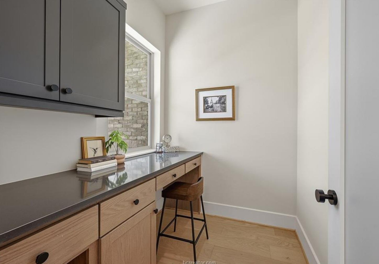 Built-in desk nook with charcoal upper cabinets, oak drawers and a window overlooking brick.