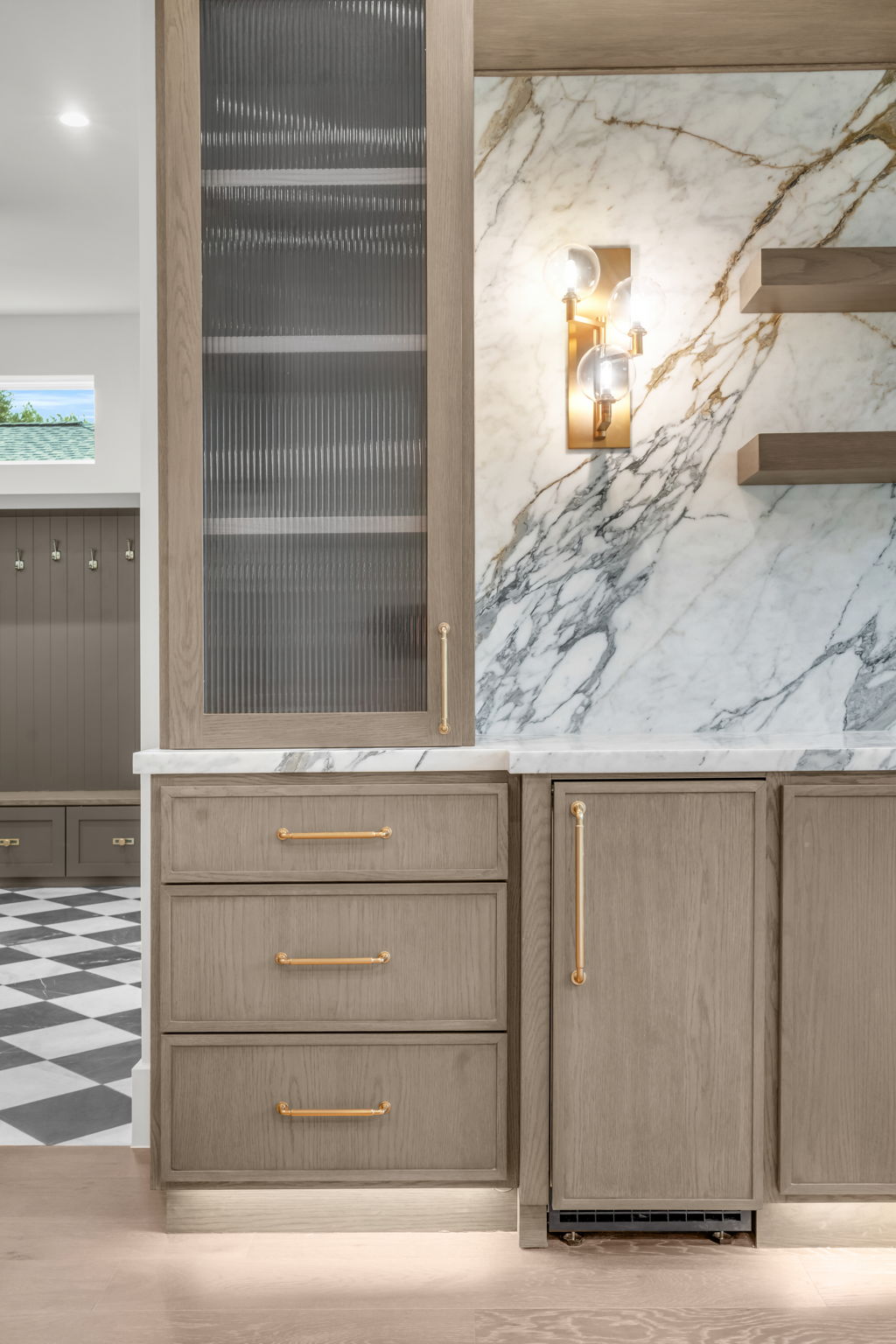 A custom kitchen with light wood cabinetry, veined marble surfaces, and brass hardware.