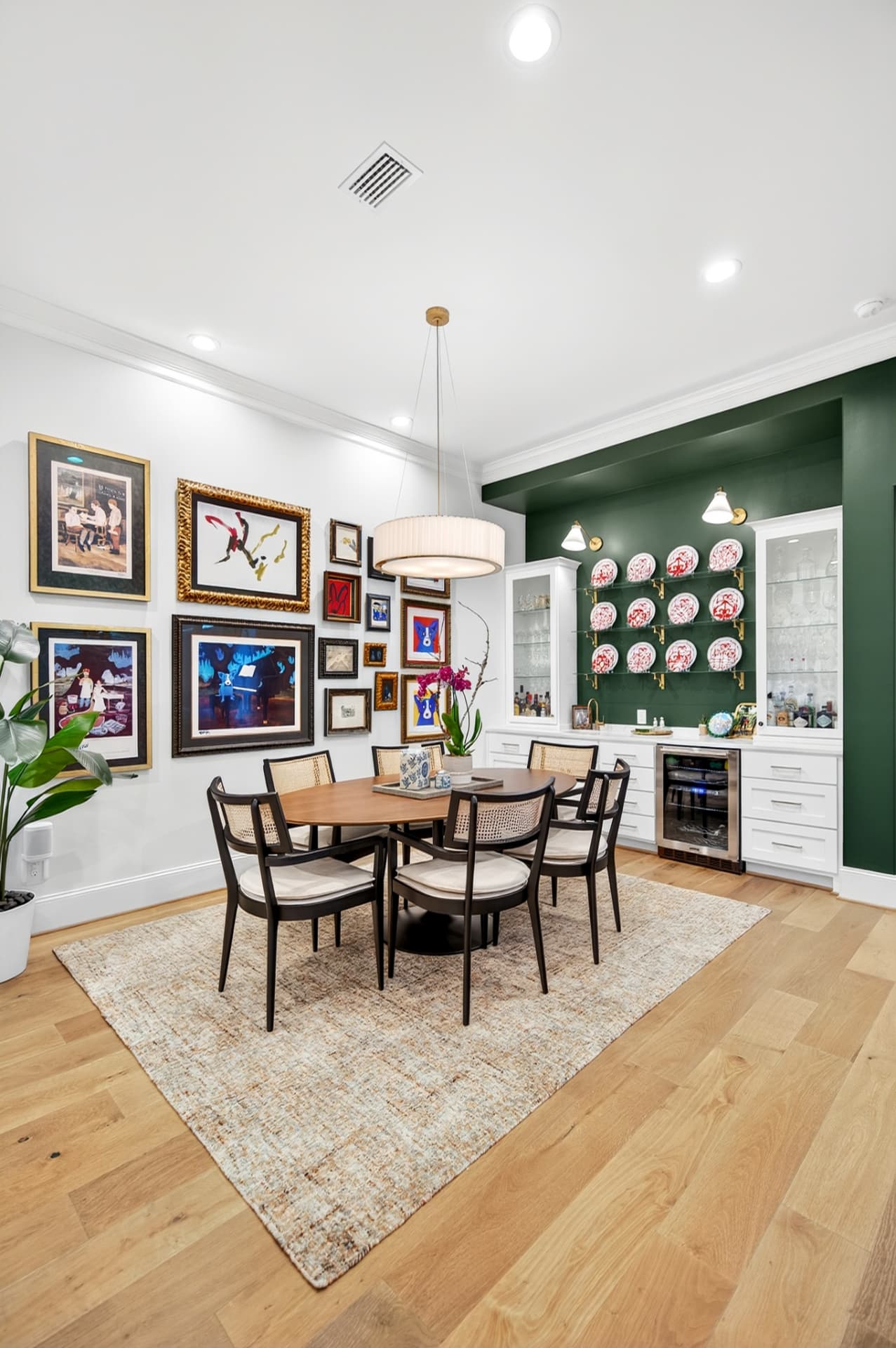 Dining room with a salon-style art wall, green built-in bar and a round walnut table with cane chairs.