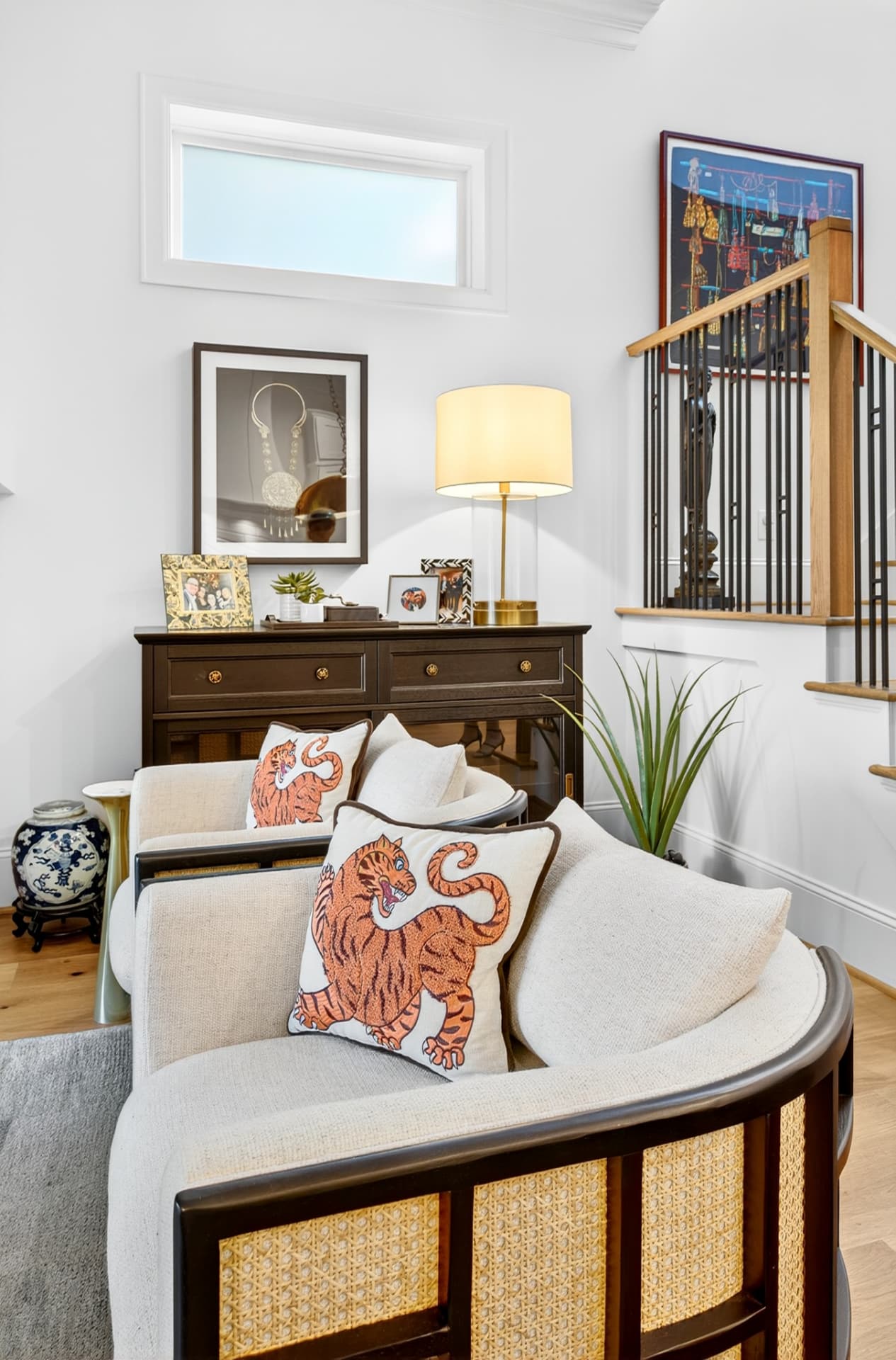 Sitting area with curved cane-back chairs, embroidered tiger pillows and a dark wood console.