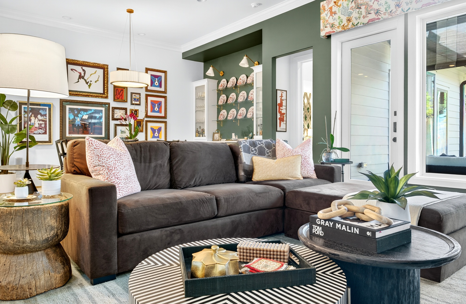 A completed living room with a deep green accent wall, a curated gallery wall, layered textiles on a rich sectional sofa, and natural light from tall windows.