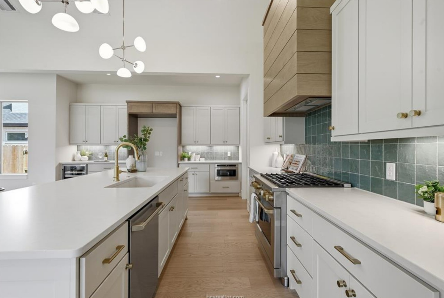 Bright kitchen with white shaker cabinetry, a white oak hood, green tile backsplash and brass hardware.